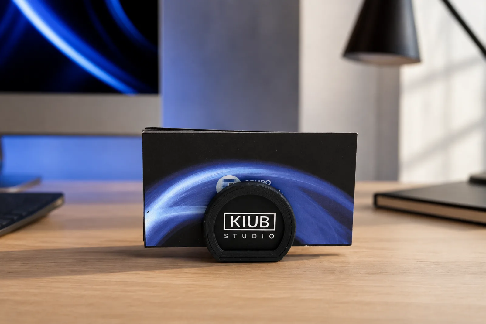 Portatarjetas negro con el logo de Kiub Studio, sosteniendo un taco de tarjetas de presentación sobre un escritorio.
