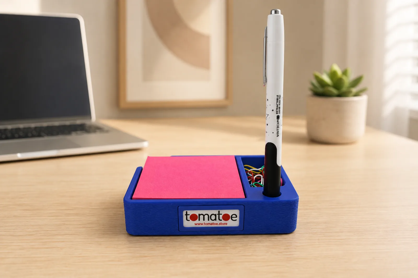 Organizador de escritorio azul con notas adhesivas, clips y una pluma, con una placa al frente con el logo de la marca tomatoe.